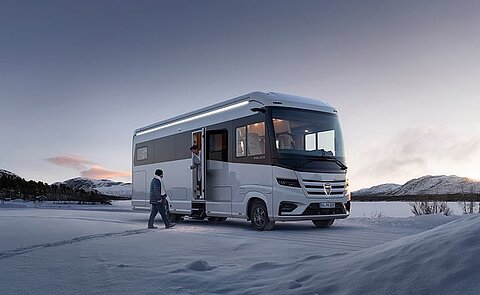 Ein Morelo Palace Wohnmobil geparkt in einer Schneelandschaft. Davor ein Pärchen im Eingangsbereich.