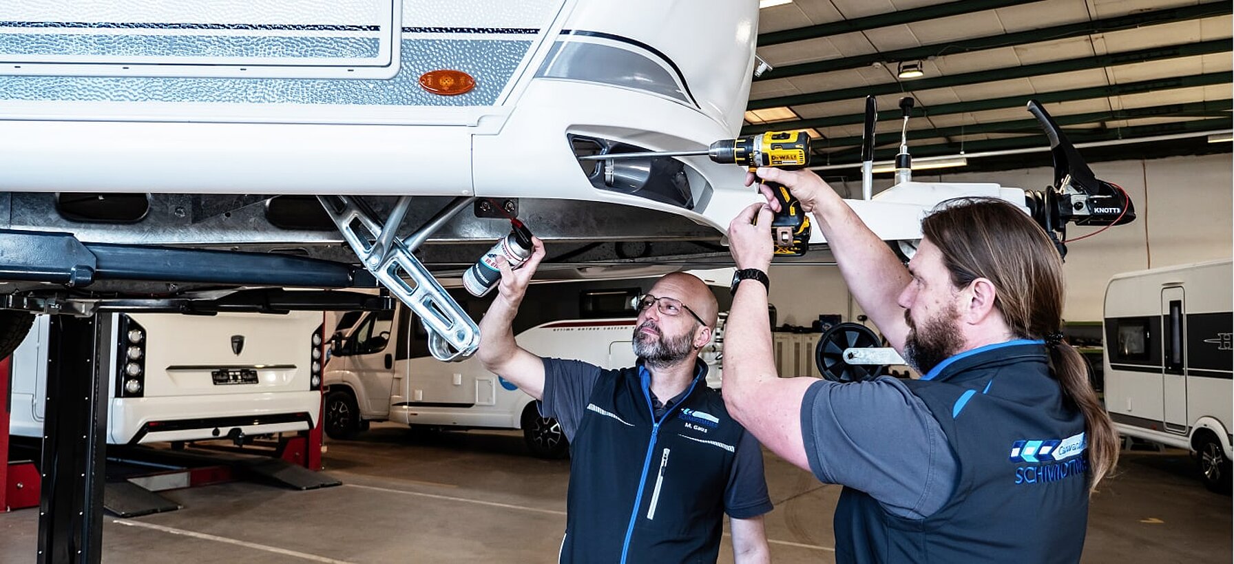 Zwei Werkstattmitarbeiter von Caravaning Center Schmidtmeier bei der Arbeit an einem Wohnwagen auf einer Hebebühne.
