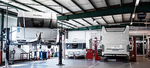 Blick in die Werkstatt von Caravaning Center Schmidtmeier und Sicht auf mehrere Hobby Wohnwagen, einen Beachy Wohnwagen sowie ein Wohnmobil von Morelo.
