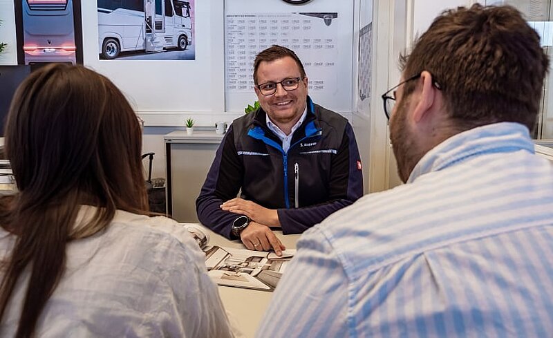 Beratungsgespräch zwischen einem Verkaufsberater von Caravaning Center Schmidtmeier und einem interessierten Pärchen in einem Büro. Beratungsgespräch zwischen einem Verkaufsberater von Caravaning Center Schmidtmeier und einem interessierten Pärchen in einem Büro.