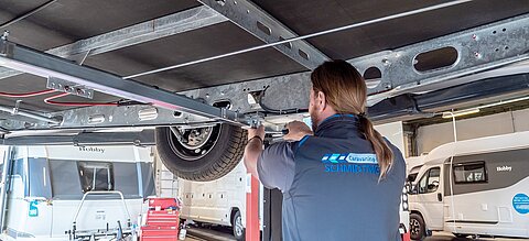 Ein Werkstattmitarbeiter von Caravaning Center Schmidtmeier bei der Arbeit an einem Wohnwagen auf einer Hebebühne.