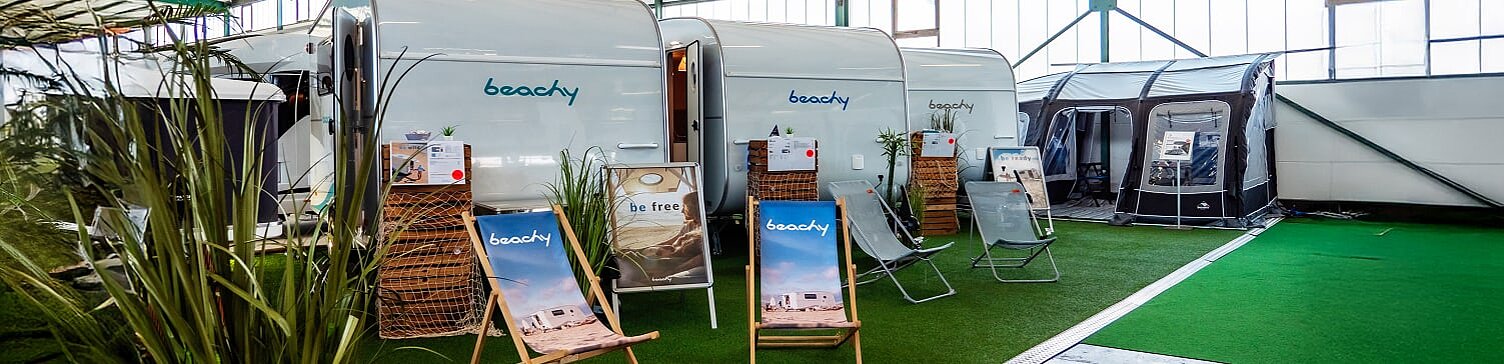 Drei beachy Wohnwagen nebeneinander mit aufgebauten Liegestühlen in der Ausstellungshalle von Caravaning Center Schmidtmeier