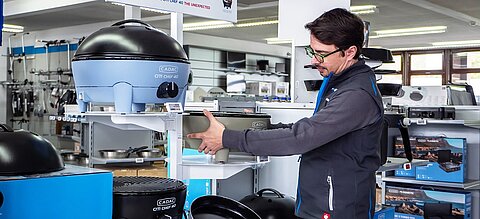 Ein Shop-Mitarbeiter von Caravaning Center Schmidtmeier räumt ein Regal mit Cadac-Campinggrills ein.