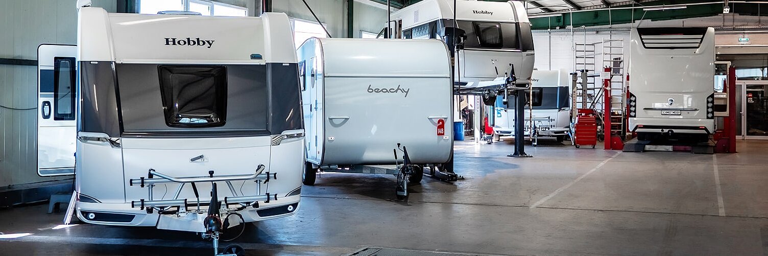 Blick in die Werkstatt von Caravaning Center Schmidtmeier und Sicht auf mehrere Hobby Wohnwagen, einen Beachy Wohnwagen sowie ein Wohnmobil von Morelo.