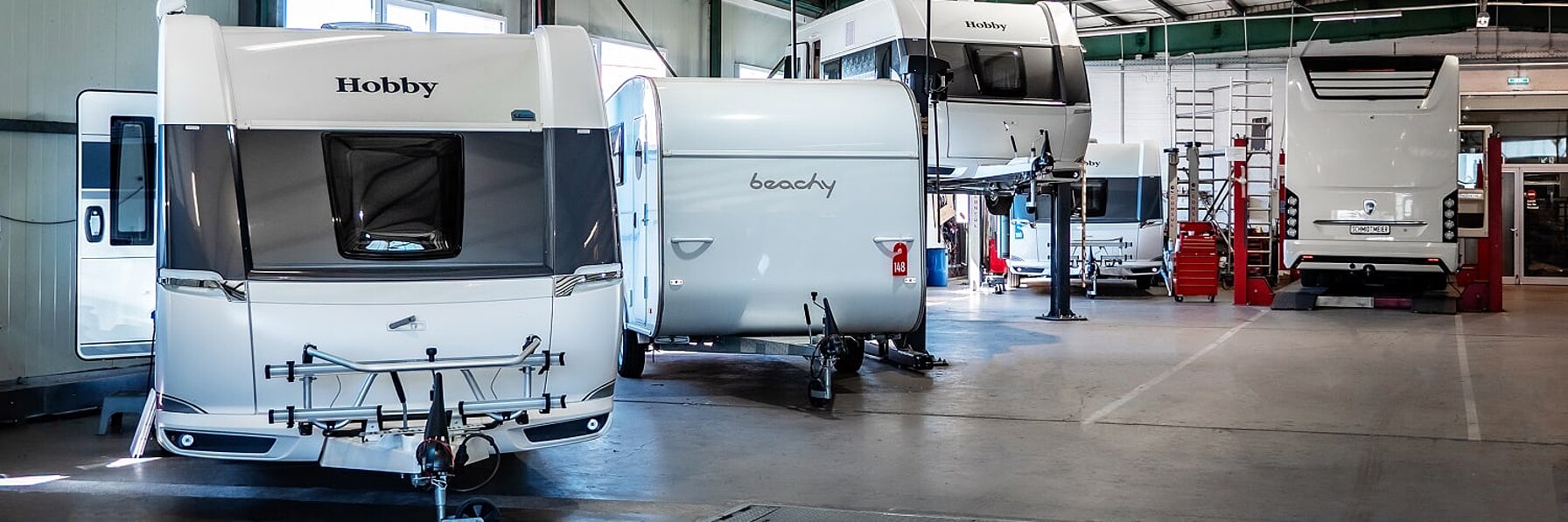 Blick in die Werkstatt von Caravaning Center Schmidtmeier und Sicht auf mehrere Hobby Wohnwagen, einen Beachy Wohnwagen sowie ein Wohnmobil von Morelo.