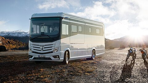 Ein weißes Morelo Wohnmobil geparkt auf einem Schotterplatz, daneben zwei Motorräder.