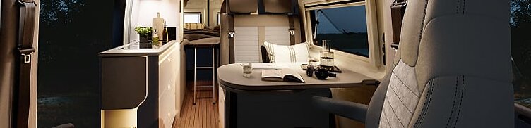Innenansicht des Kastenwagens Hobby Prestige Van mit Blick in den Essbereich vom Cockpit aus bei Nacht.
